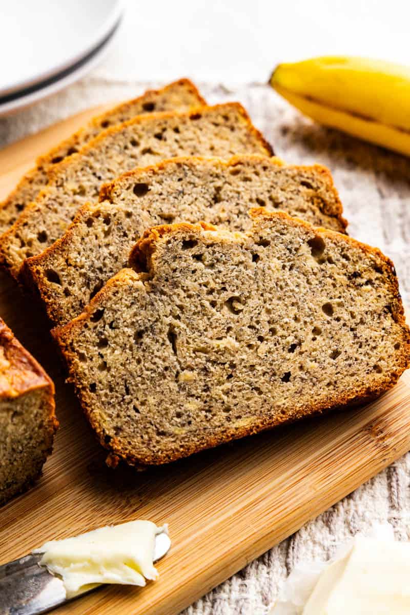 Slices of banana bread laying against each other like fallen dominoes on a cutting board.