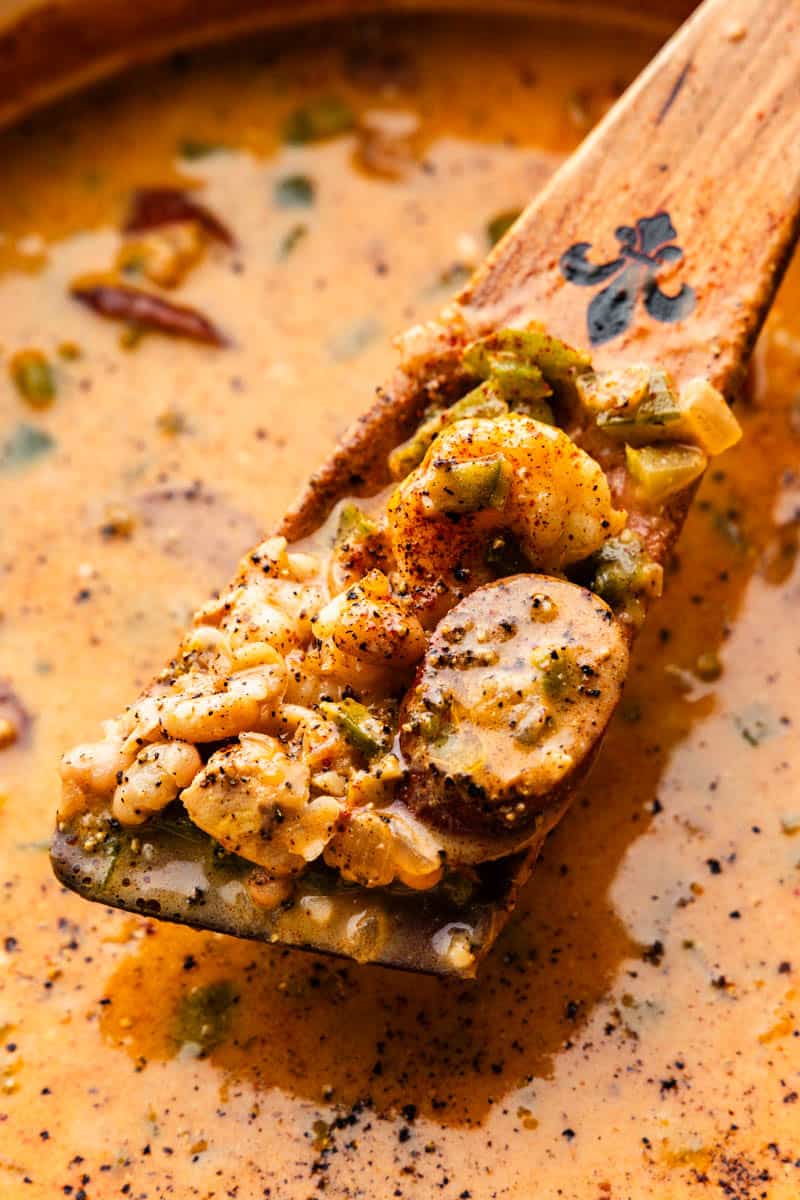 A roux spoon lifting out a serving of Cajun white chicken chili from the pot.