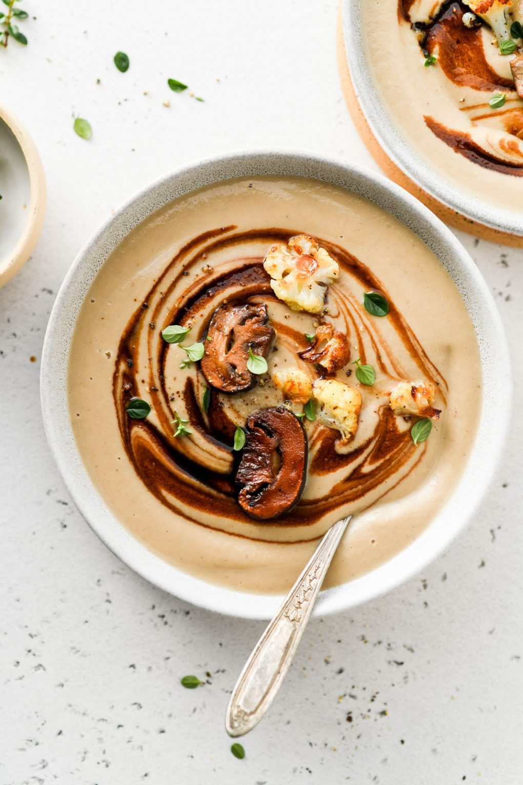 A bowl of creamy cauliflower and mushroom soup is topped with mushrooms, cauliflower, and herbs.