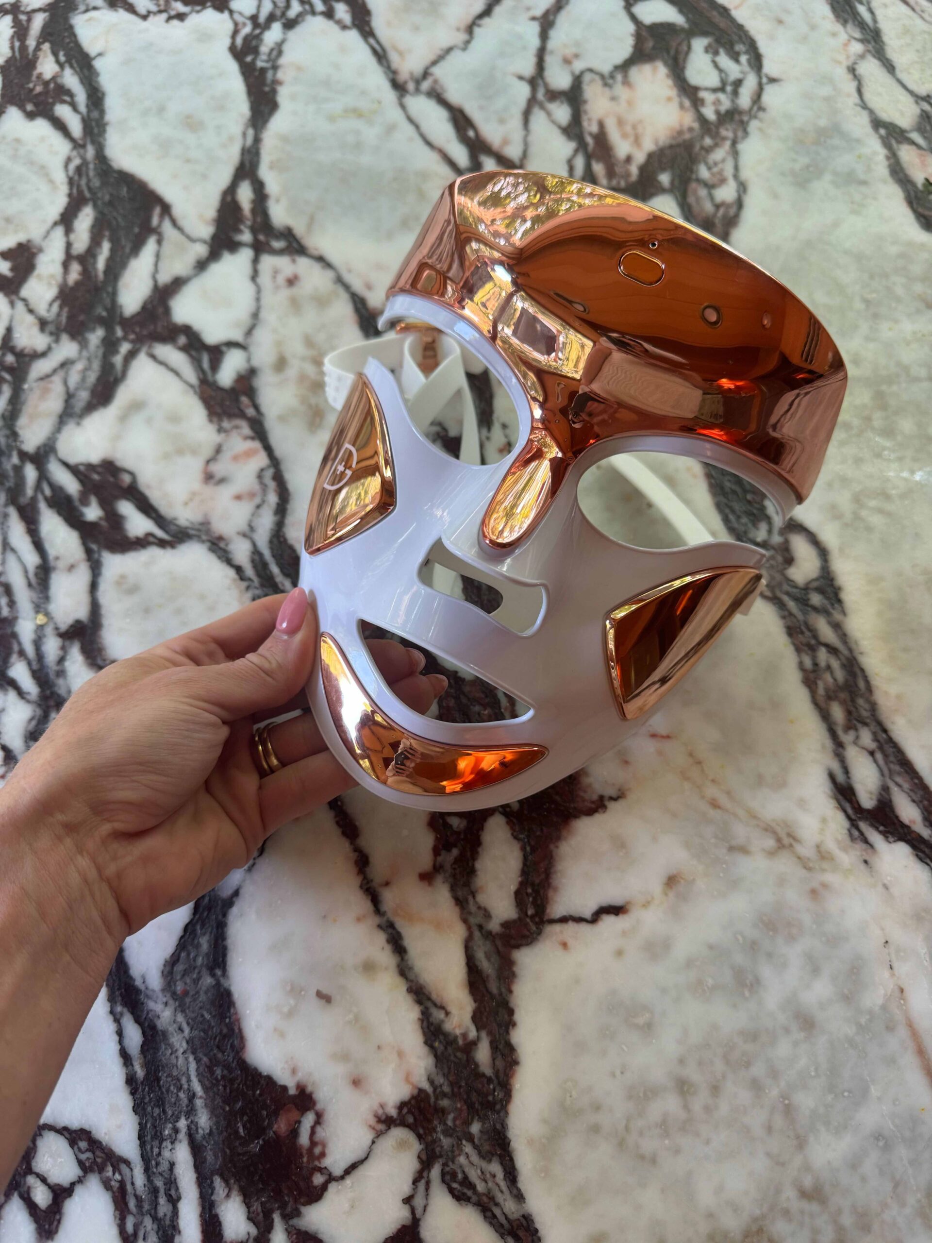 The Dr. Dennis Gross LED mask is powered off and held over a marble countertop