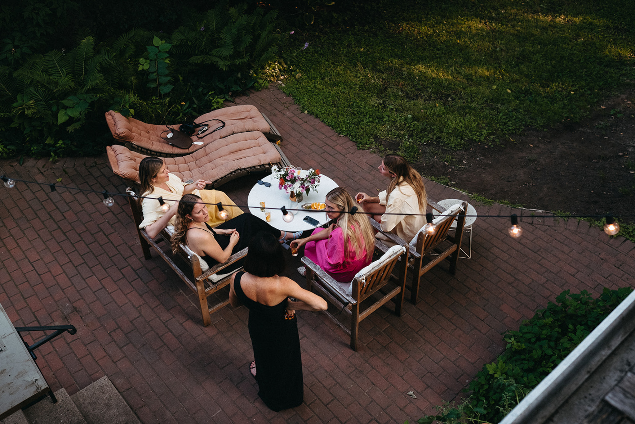 Five friends gather for a casual dinner party. They're pictured sitting on a brick patio, drinking vermouth spritz cocktails, and chatting before dinner.