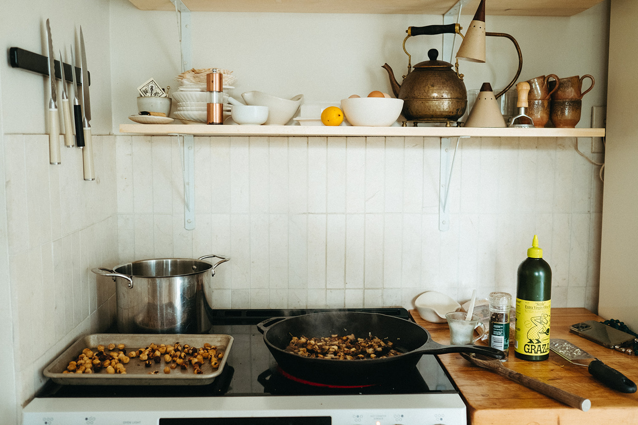 A cooking nook in a kitchen, with hazelnuts toasting on the stovetop. On the adjacent countertop are cooking tools, olive oil, and salt and pepper.