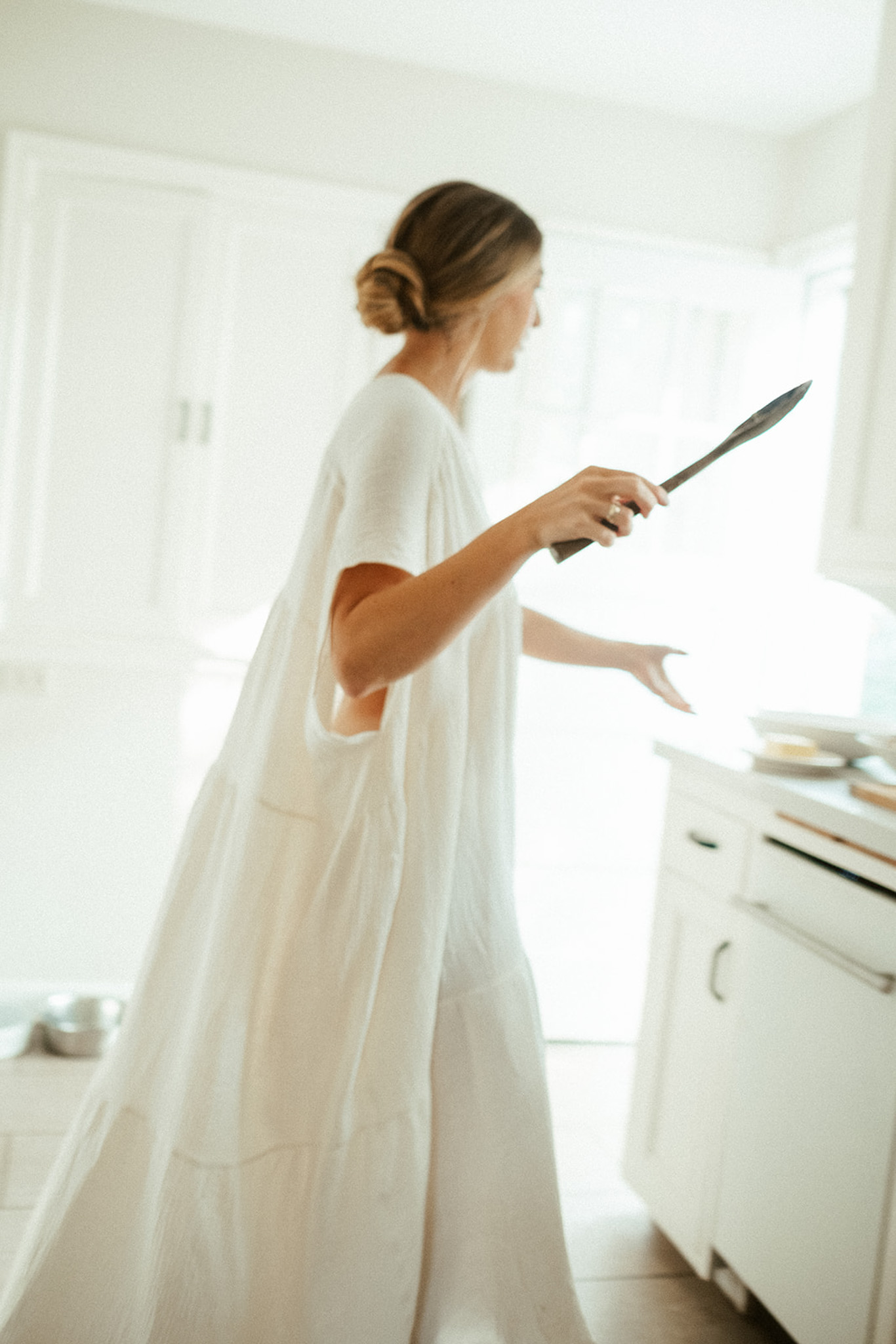 A woman is walking through a kitchen wearing a long, flowing white dress.