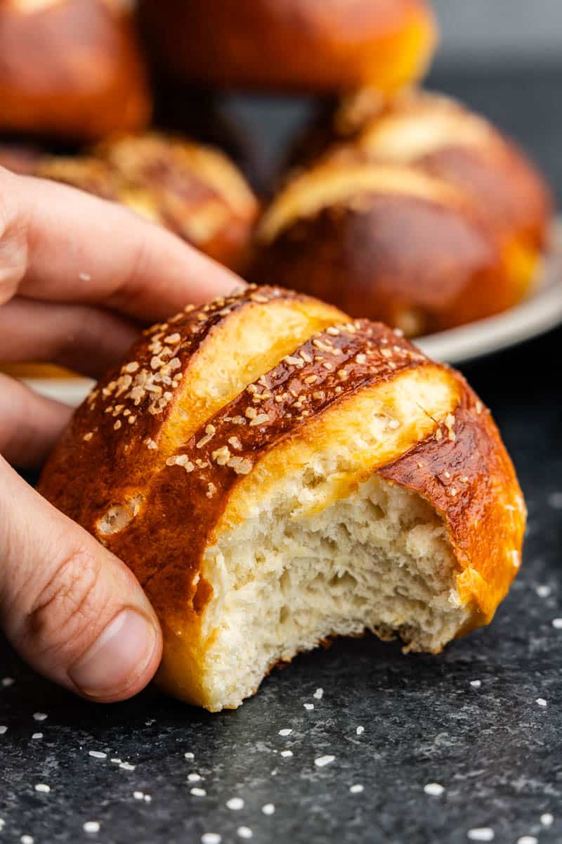 A close up view of a hand holding a homemade pretzel roll that has had a bite taken out of it.