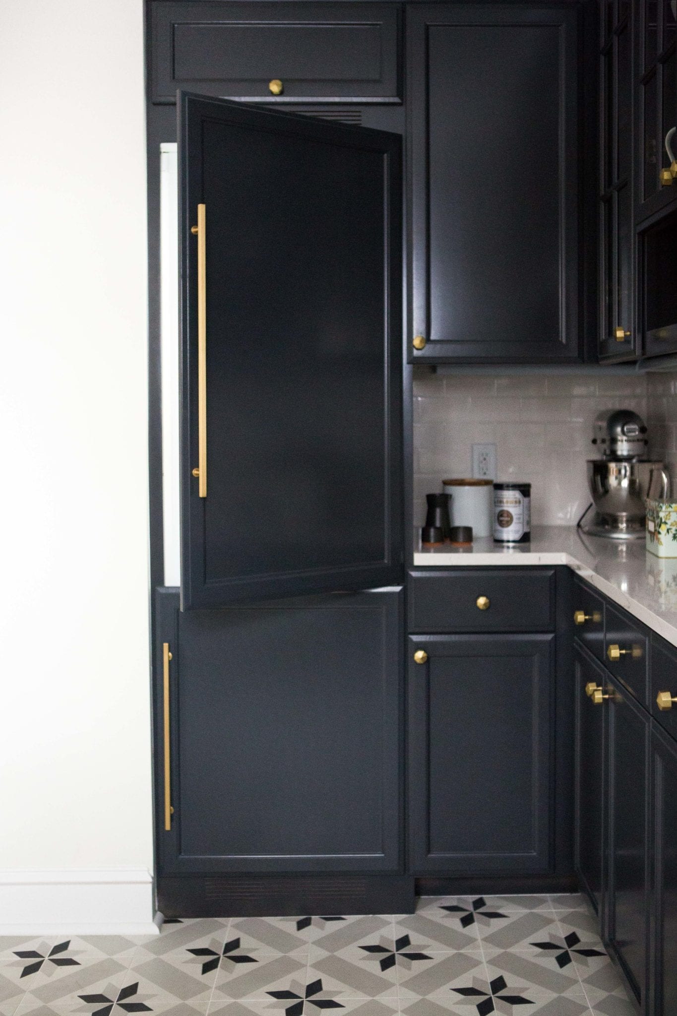 A modern kitchen has cabinets painted in Wrought Iron by Benjamin Moore, marble countertops, and subway tile backsplash.