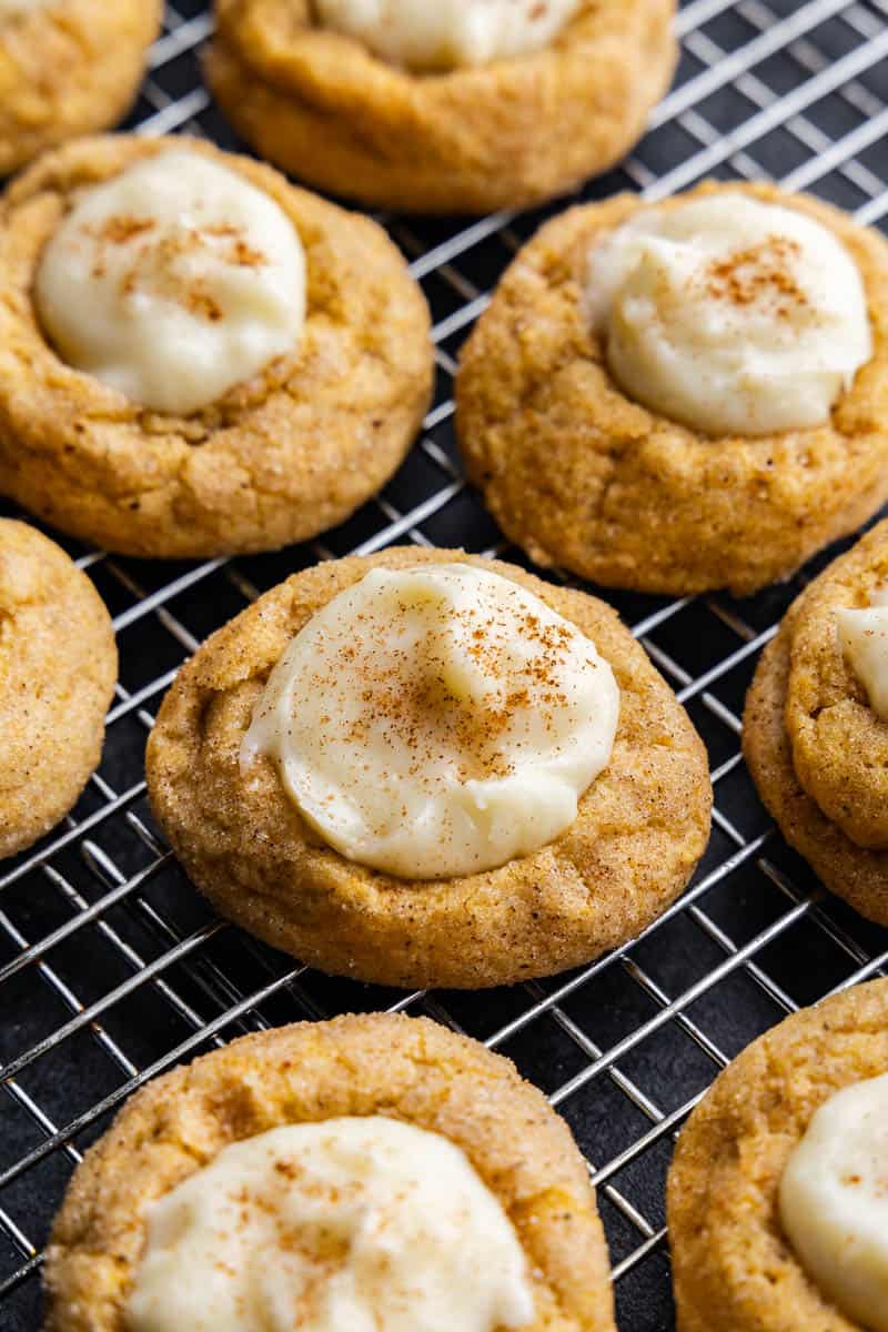 A closeup view of pumpkin cheesecake thumbprint cookies on a wire cooling rack.