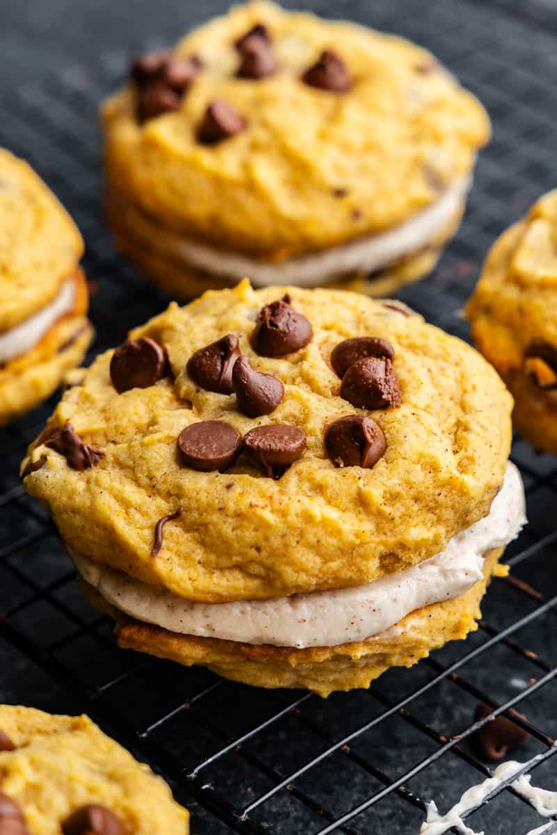 A close up of a pumpkin chocolate chip cookie sandwich with a cream filling.