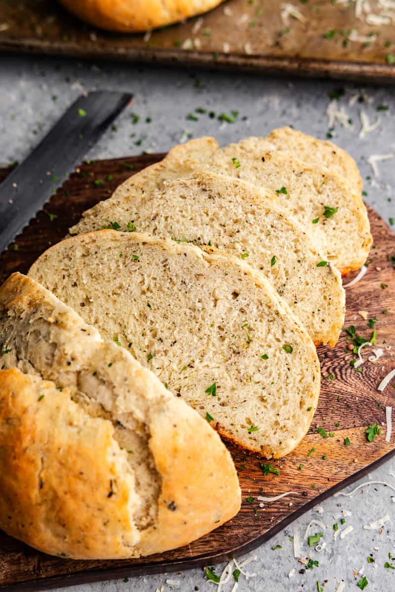 An overhead view of a loaf of garlic parmesan herb bread that has been sliced on a cutting board.