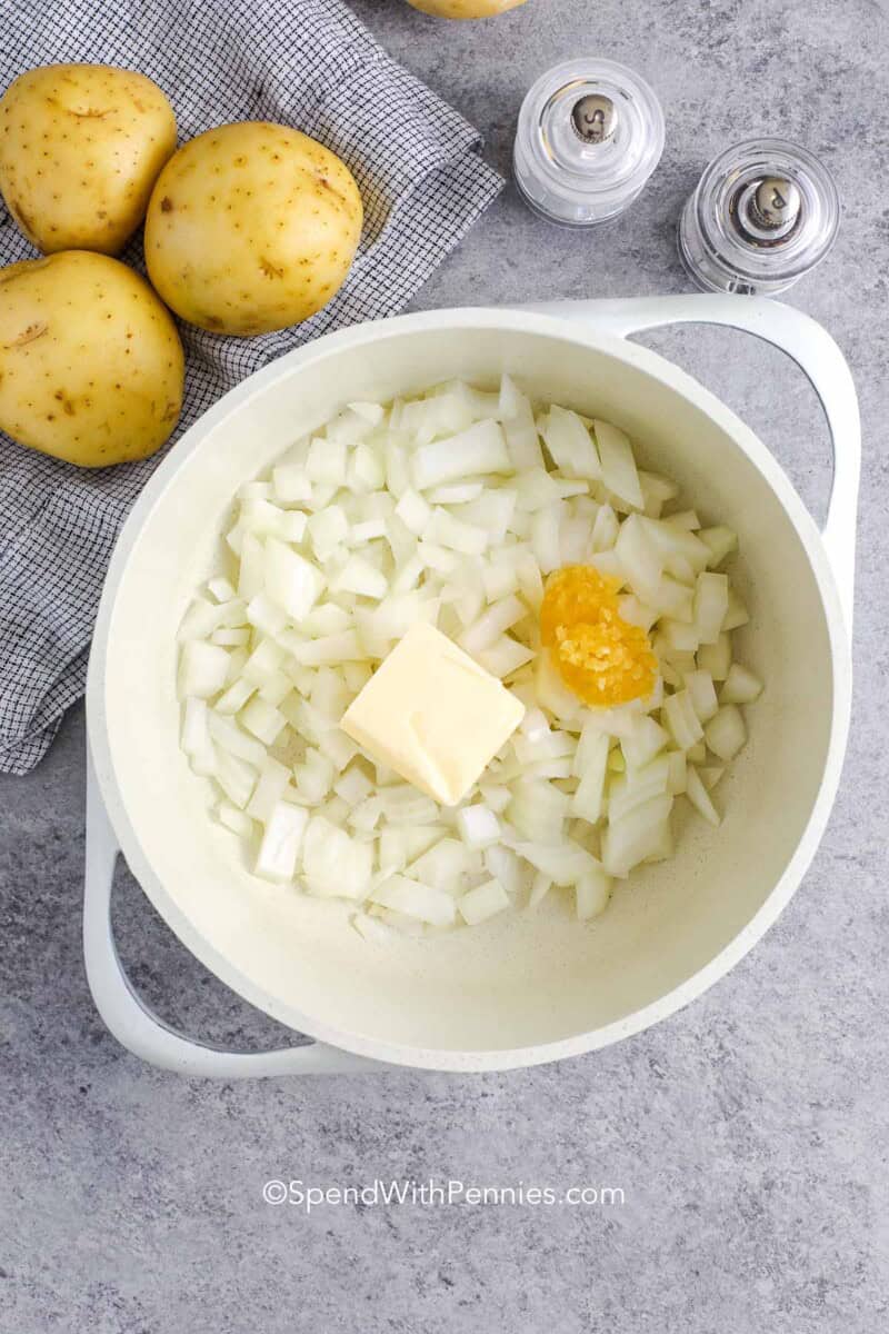 Uncooked onions, butter, garlic in a small pot for making scalloped potatoes sauce