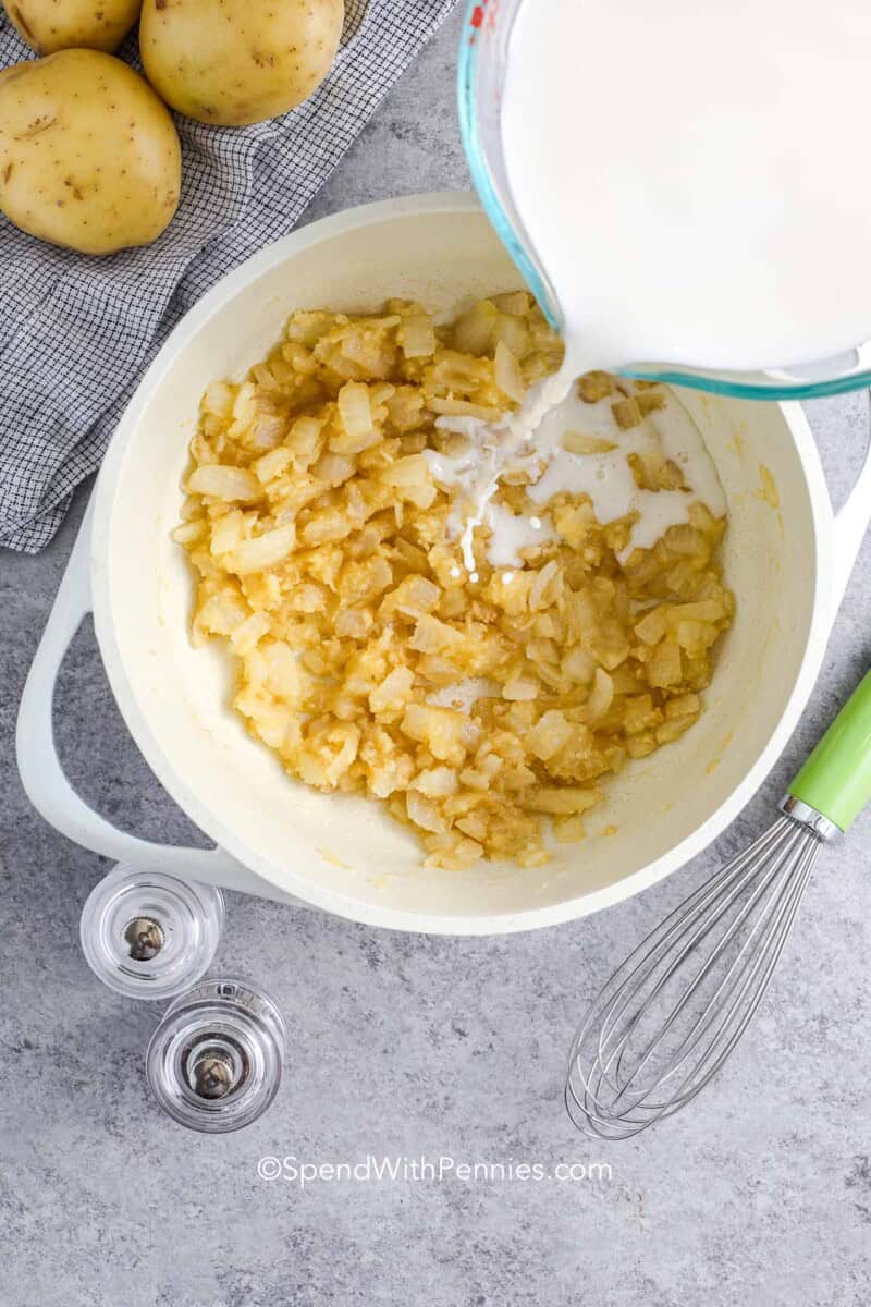 Adding milk to cooked onions in a small pot for making scalloped potatoes sauce