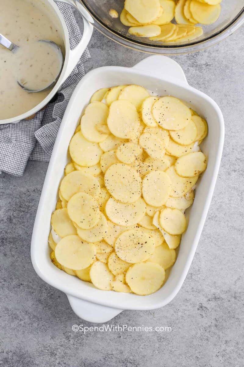 Thinly sliced potatoes in a white casserole dish next to sauce