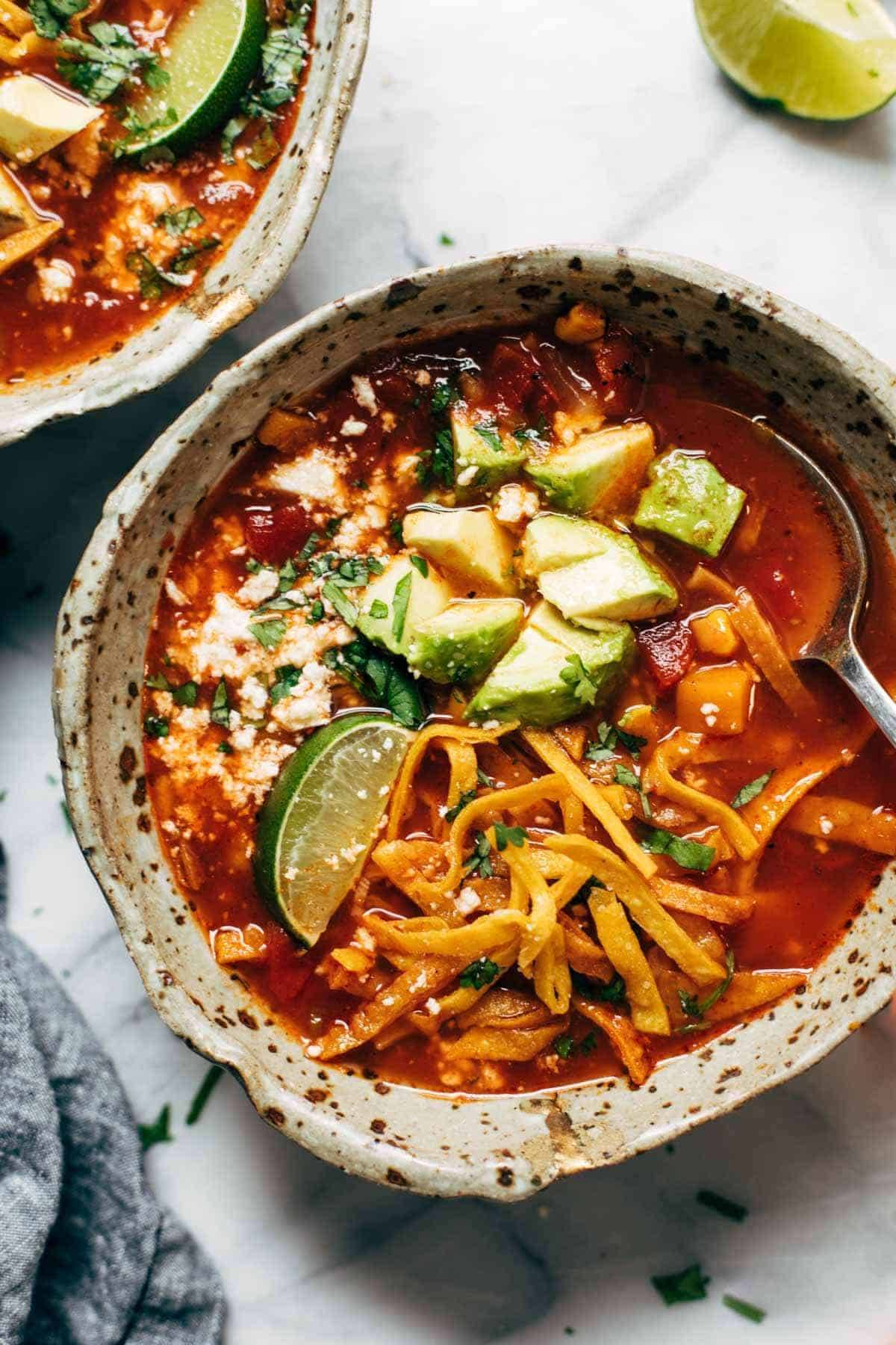 Fall soup recipes: A bowl of sweet potato tortilla soup is topped with lime, avocado, cheese, and tortilla strips.