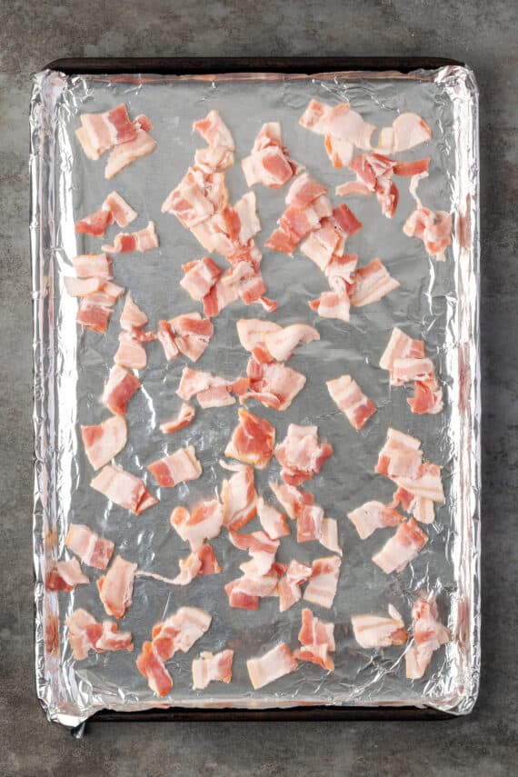 Diced bacon scattered over a baking sheet lined with foil.