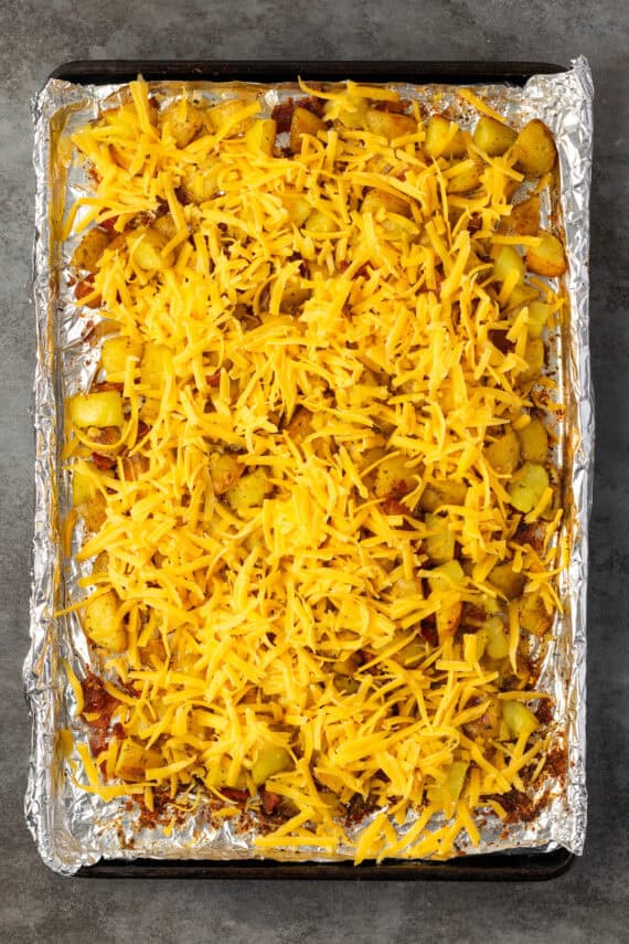 Roasted ranch potatoes topped with shredded cheese on a lined baking sheet.