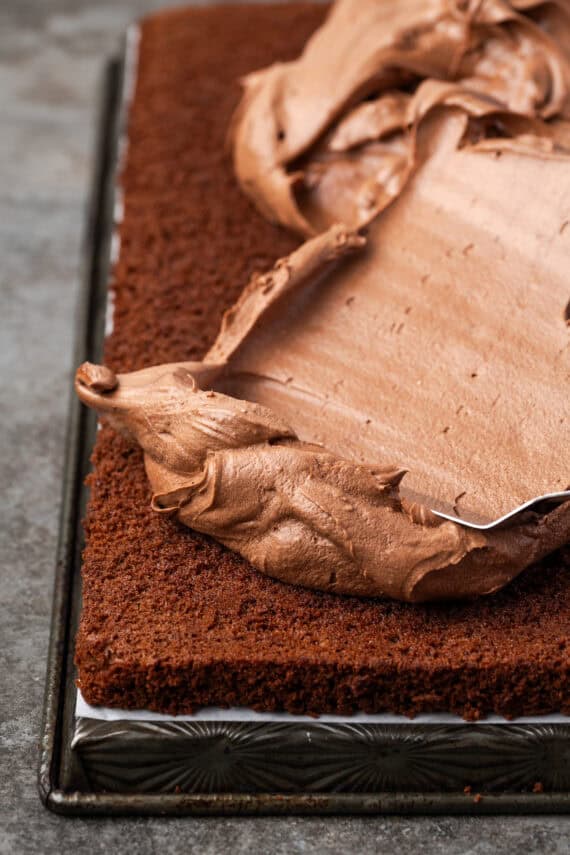 Chocolate frosting partially spread over top of a chocolate cake layer.