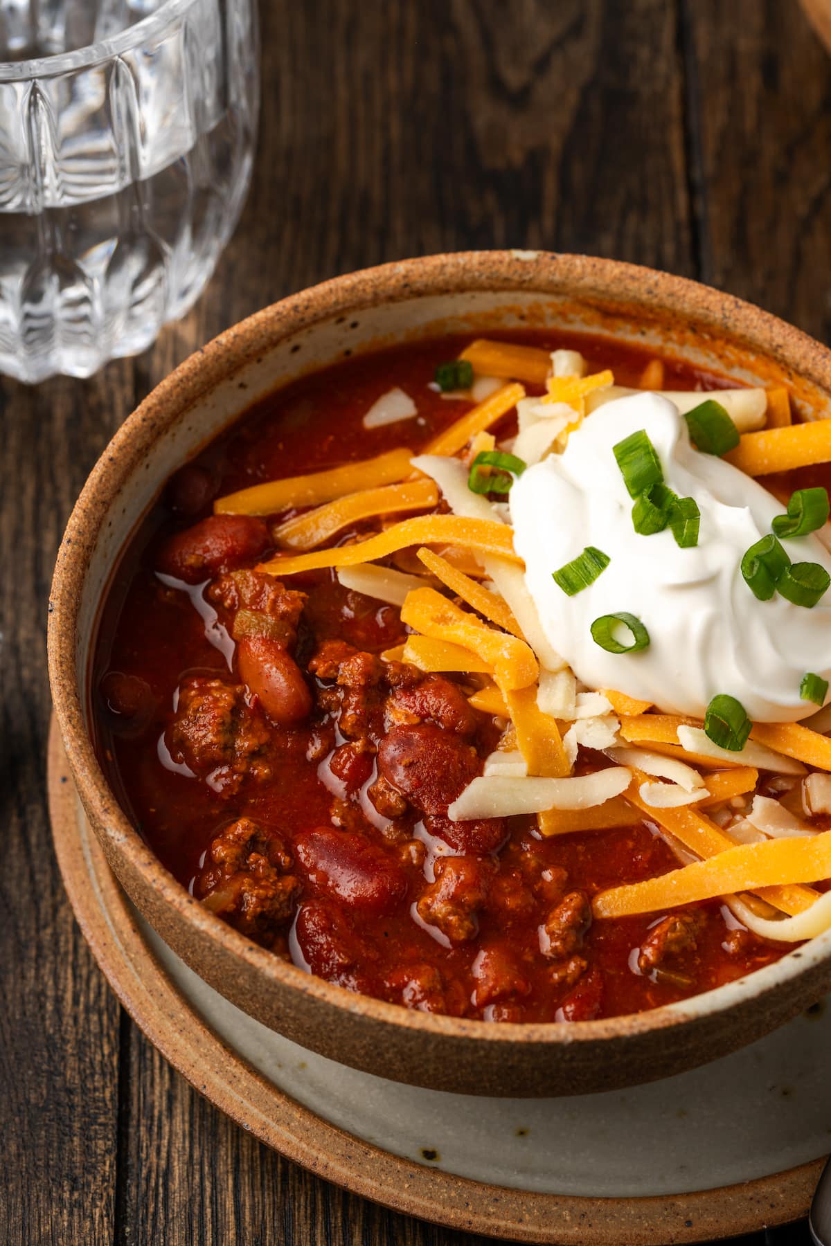 Instant pot chili garnished with shredded cheese, sour cream, and chives in a stoneware bowl.