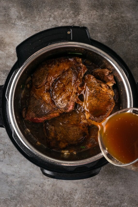 Beef stock is poured over chuck roast and sauteed onions inside the instant pot.