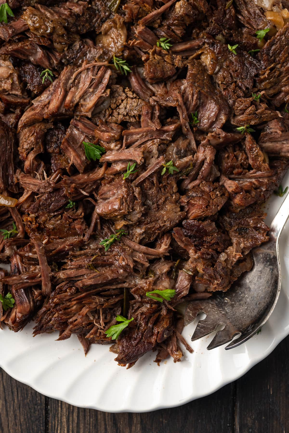 Shredded instant pot chuck roast on a white plate next to a serving spoon.