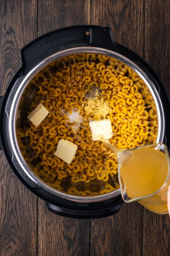 Chicken stock being poured over macaroni noodles, seasonings, and butter in the Instant Pot.