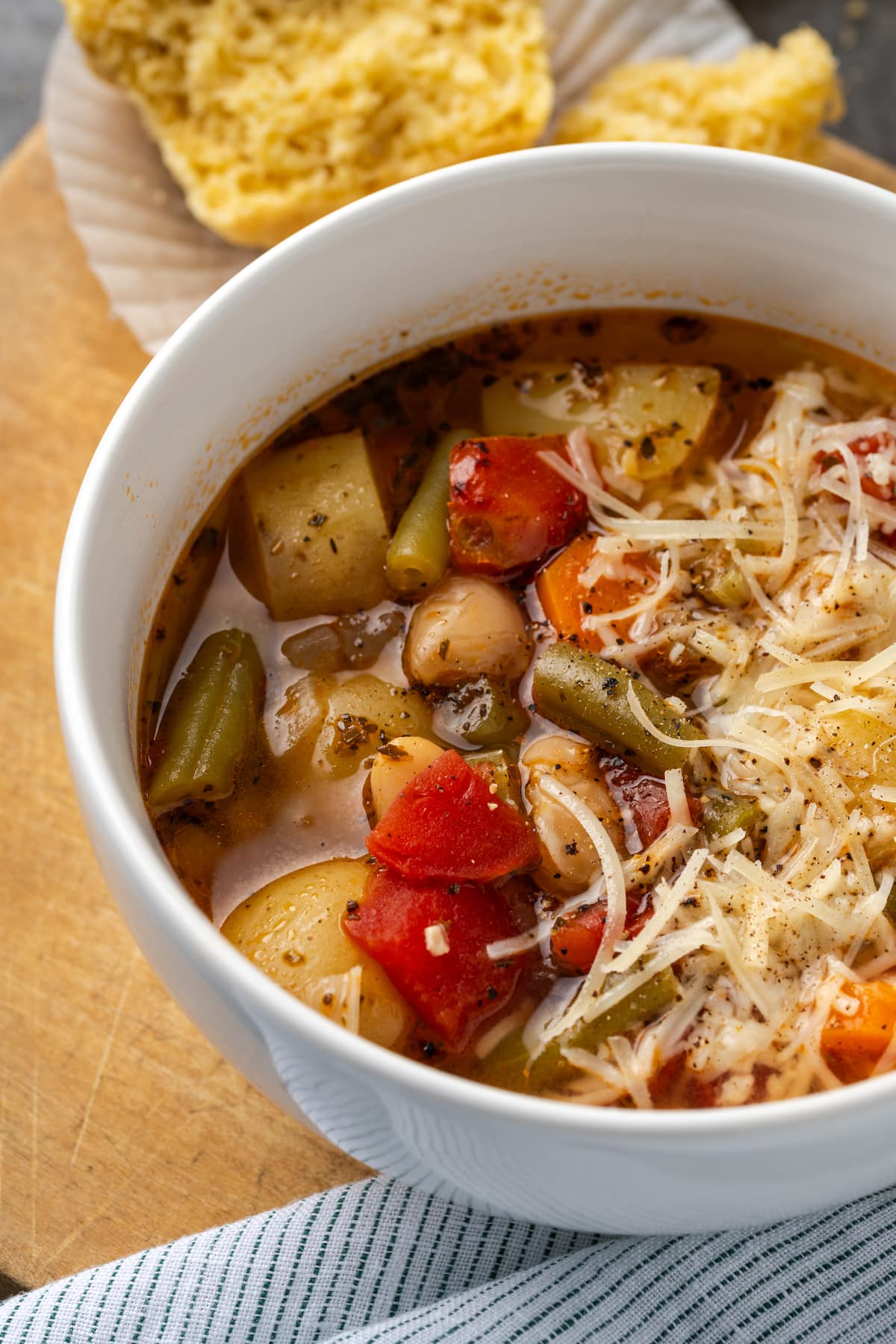 A bowl of instant pot vegetable soup with a cornbread muffin in the background.