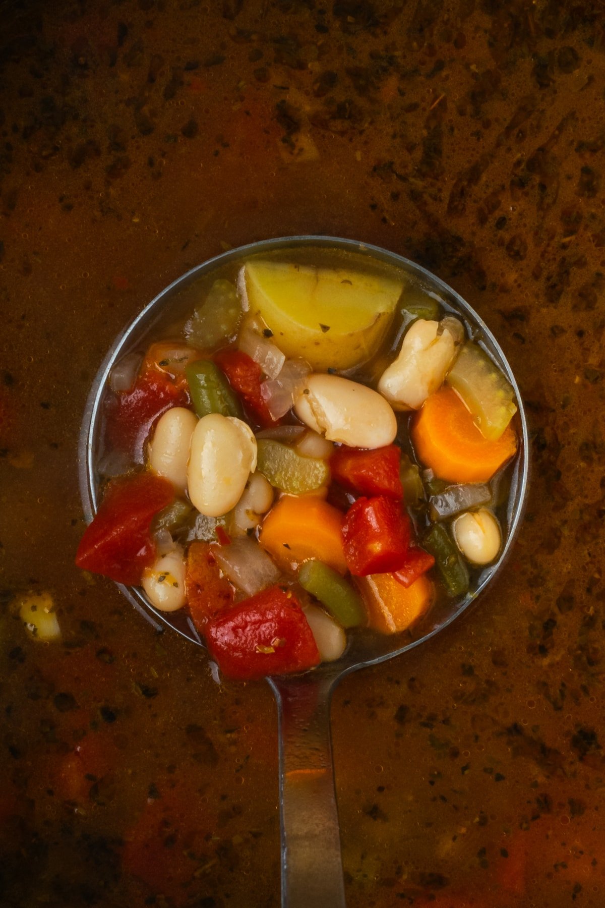 Overhead view of a ladleful of vegetable soup held over the instant pot.