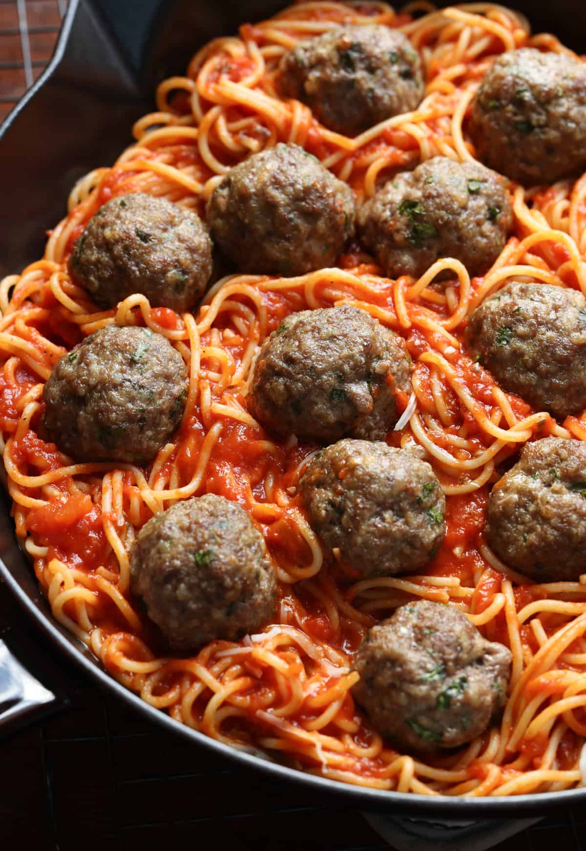 Assembling baked spaghetti topped with sauce and meatballs in a skillet.