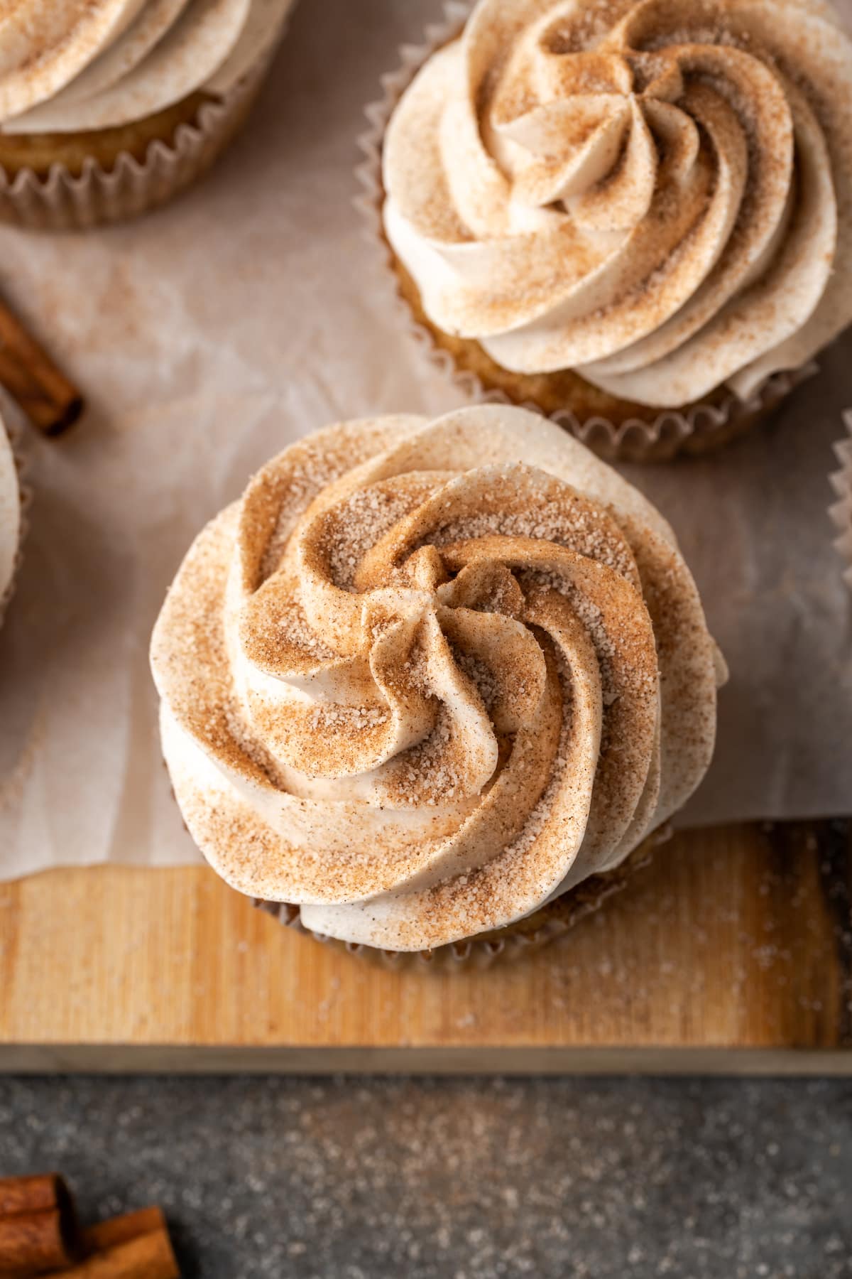 Close up overhead view of snickerdoodle cupcakes topped with swirls of cinnamon buttercream frosting on a wooden cutting board.