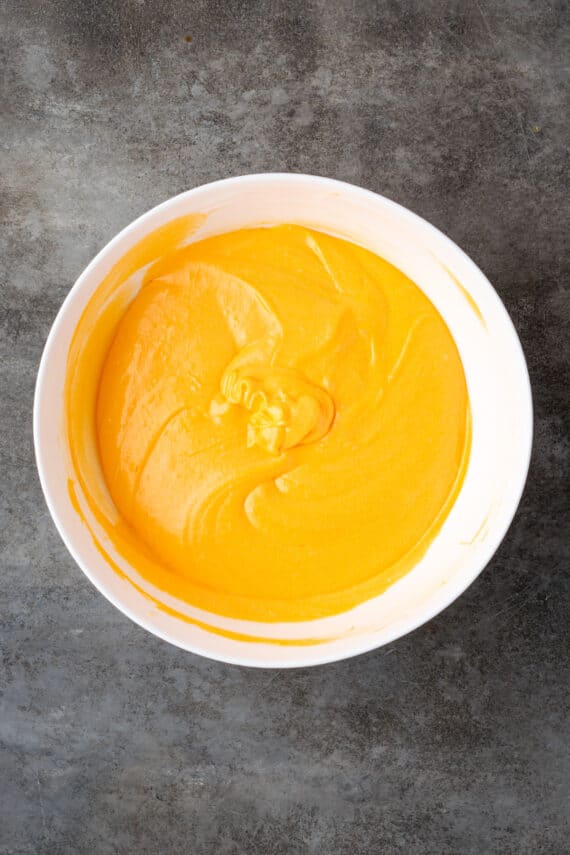 Cake batter colored orange in a large white mixing bowl.