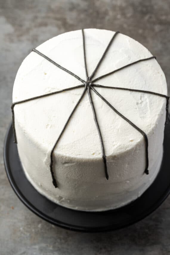 Black spider web lines piped over a white frosted layer cake.