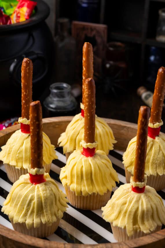 Witch's broom Halloween cupcakes on a wooden platter lined with black and white striped paper.