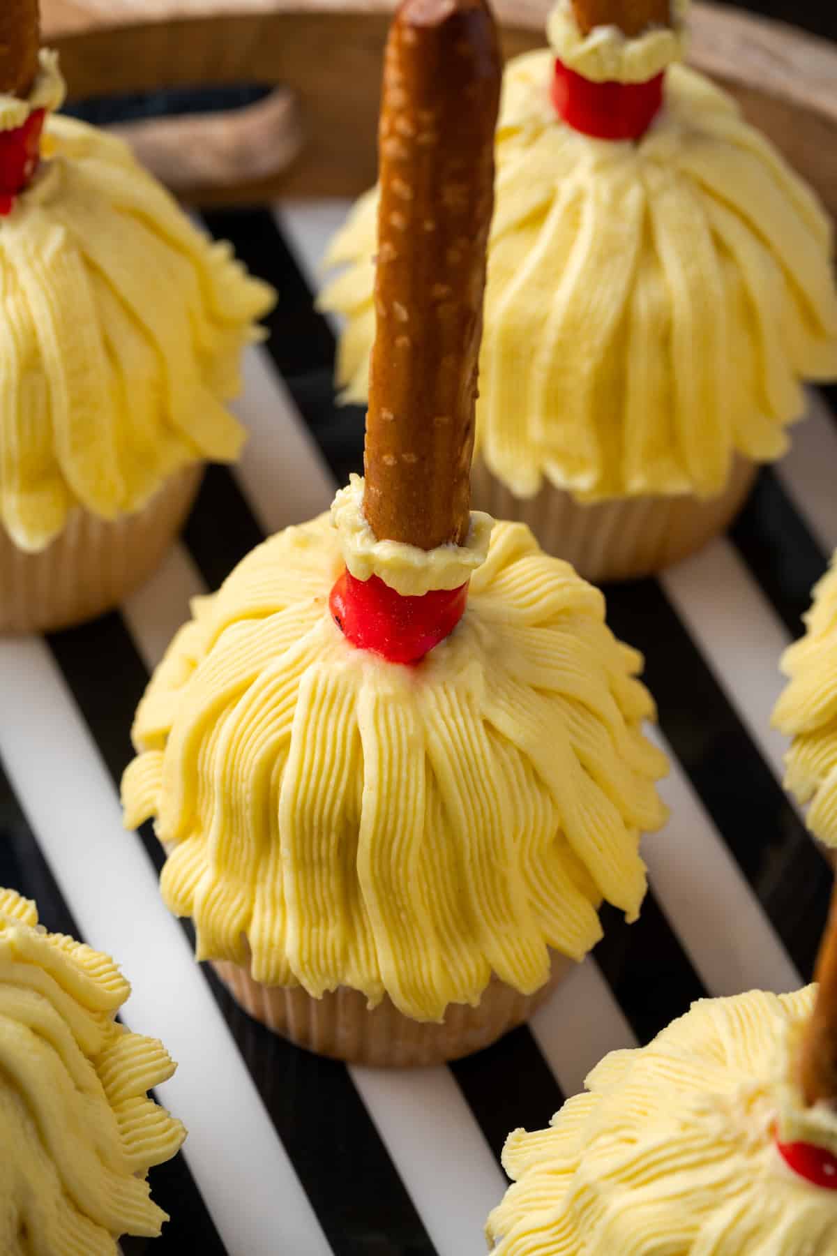 Close up of witch's broom Halloween cupcakes on a wooden platter lined with black and white striped paper.